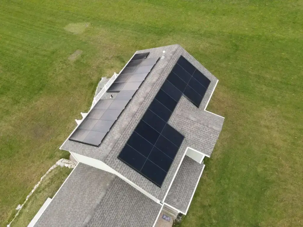Aerial view of a residential solar panel installation by Premier Improvements Solar in Connecticut, featuring sleek all-black panels installed on a gray-shingled roof surrounded by green lawn. This efficient rooftop solar system is designed to maximize sunlight exposure and reduce electricity costs.